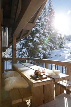 a wooden table sitting on top of a snow covered porch next to a forest filled with trees