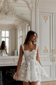 a woman in a short white dress is standing near a mirror