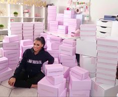 a woman is sitting on the floor surrounded by pink boxes that are stacked high up