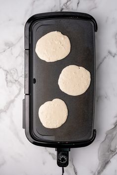 three uncooked hamburger patties in a black pan on a marble countertop