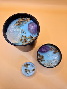 two black bowls filled with blue liquid and some dried flowers on the table next to them