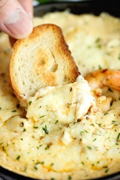 a hand dipping some bread into a bowl of dip with shrimp and cheese on top