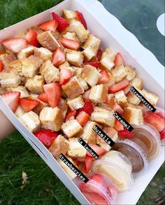 a box filled with sliced strawberries and cubes of cake next to two cups