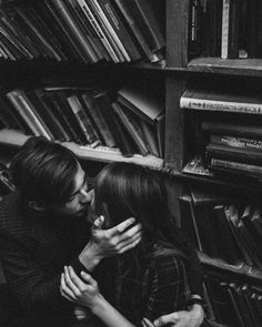 black and white photo of two people kissing in front of bookshelves with stacks of books behind them