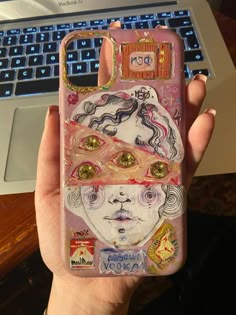 a person holding up a phone case that has pictures on it and is next to a laptop