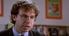 a man wearing glasses and a tie in front of bookshelves with posters on the wall