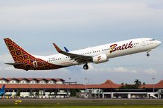 a large passenger jet taking off from an airport runway with buildings in the back ground