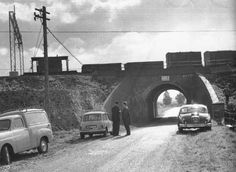 an old black and white photo of two men standing in front of cars on a road