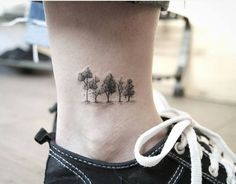 a small tree tattoo on the side of a woman's ankle, with trees in the background