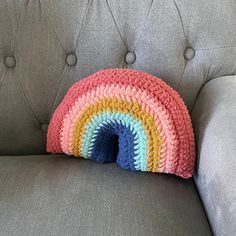 a crocheted rainbow pillow sitting on top of a gray couch