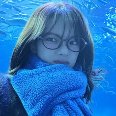 a woman wearing glasses and a blue towel in front of a fish tank at the zoo