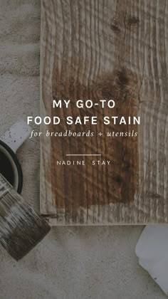 a wooden table with a cup and brush on it, next to a book that says my go - to food safe stain for breadboards & utensils