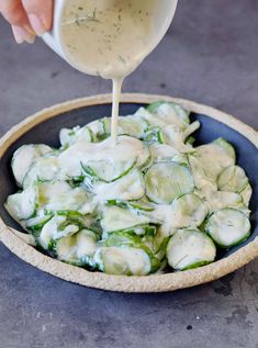 someone pouring dressing into a bowl filled with cucumbers