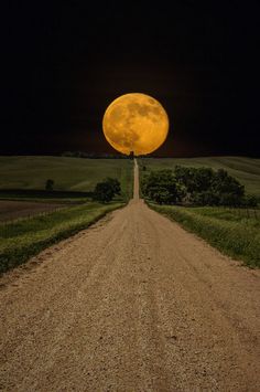 a dirt road with a full moon in the background