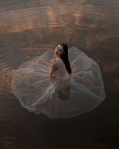 a woman floating on top of a body of water wearing a white dress and veil