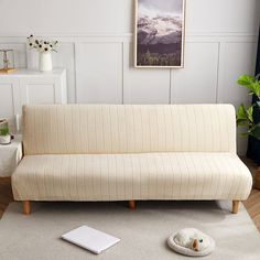 a white couch sitting on top of a wooden floor next to a rug and potted plant