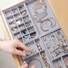 a drawer filled with lots of jewelry on top of a wooden table next to a person's hand