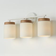 three light bathroom fixture with white glass and wood accents on the top, against a white wall