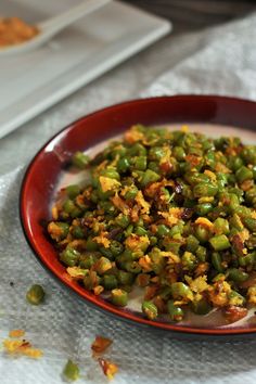 a bowl filled with green beans on top of a white cloth next to a plate full of food