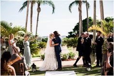 a bride and groom hug as they walk down the aisle at their wedding ceremony in front of palm trees