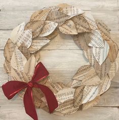 a wreath made out of old sheet music paper with a red bow on it sitting on top of a wooden table