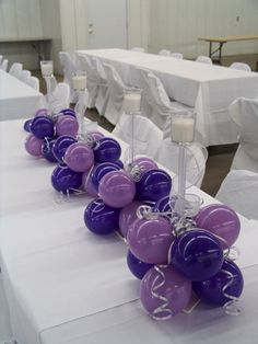 purple and white balloons sitting on top of a table in front of tables with white linens