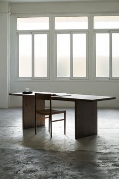 a table and chair in an empty room with large windows on the wall behind them