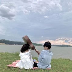 two people sitting on the grass near water