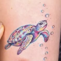 a colorful turtle tattoo on the side of a woman's thigh with water droplets around it