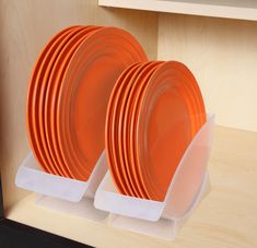 three orange plates are stacked on each other in front of a wooden shelf with white plastic holders