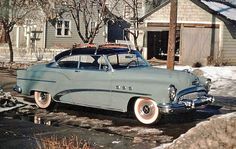 an old car parked in front of a house with snow on the ground and trees