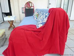 a couch covered with a red blanket on top of a tiled floor next to a table