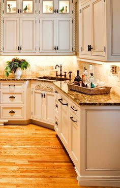 a kitchen filled with lots of white cabinets and counter top space next to a wooden floor