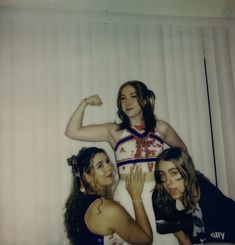 three young women posing for a photo in front of a white wall, with one woman showing off her muscles