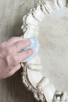 a person is using a sponge to clean the base of a large white tray on a wooden table