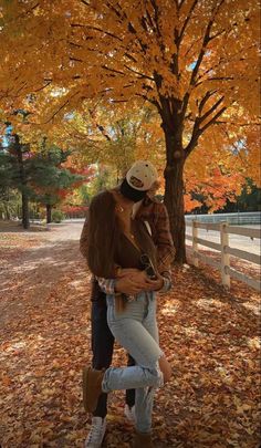 a man and woman kissing in front of a tree with fall leaves on the ground