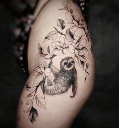 a sloth tattoo on the right side of the thigh, with leaves and flowers around it