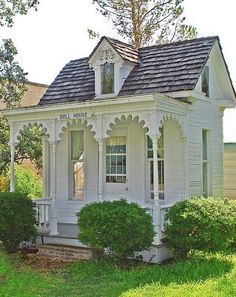 a small white house with a black roof and two dormers on the front porch