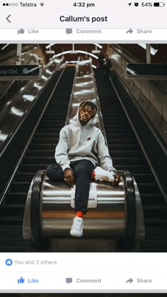 a man sitting on top of an escalator in a white sweatshirt and black pants