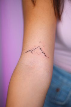 a woman's arm with a small mountain tattoo on the left side of her arm