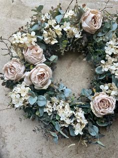 a wreath made out of flowers and greenery on a stone surface with white blooms