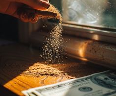 a person is sprinkling sand on top of money in front of a window