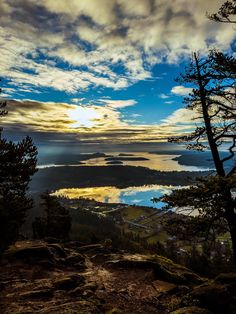 the sun is setting over some water and trees on top of a hill with mountains in the background