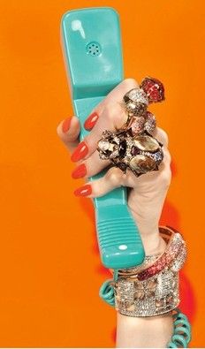 a woman's hand holding up a cell phone with multiple rings and bracelets on it