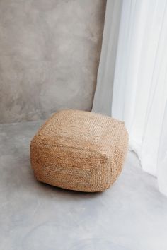 a large round ottoman sitting on top of a cement floor next to a white curtain