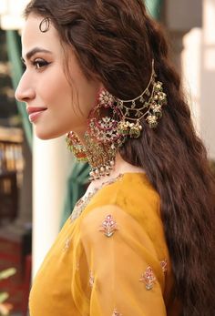 a woman with long brown hair wearing earrings and a yellow dress is looking off to the side