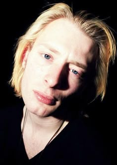 a man with blonde hair and blue eyes looking at the camera while wearing a black shirt