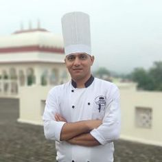 a man standing in front of a building wearing a chef's hat with his arms crossed