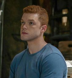 a man with red hair and blue shirt sitting on a bench in front of a window