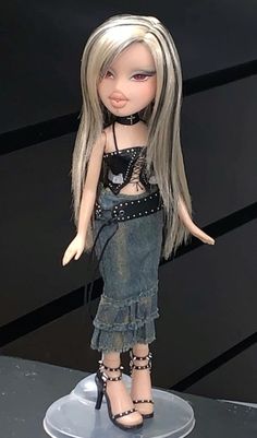 a doll with long blonde hair and black shoes on top of a white table next to a black wall